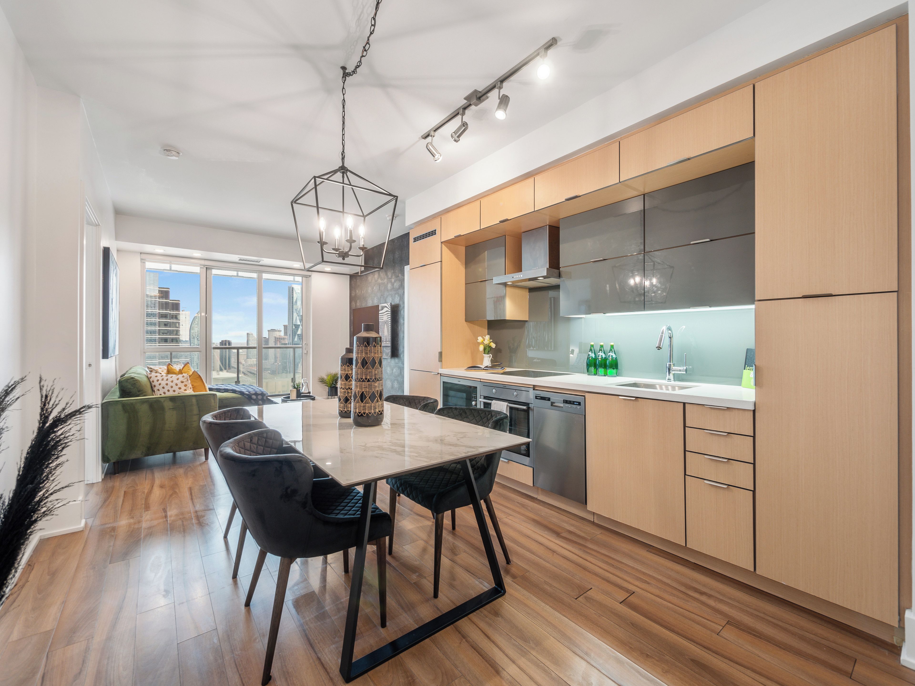 Una cocina moderna con armarios de madera, un lavamanos de acero inoxidable y una zona de comedor con una mesa de mármol y sillas negras.