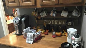 En køkkenbordplade med kaffemaskine, kopper, en mælkekande og efterårsdekorationer.