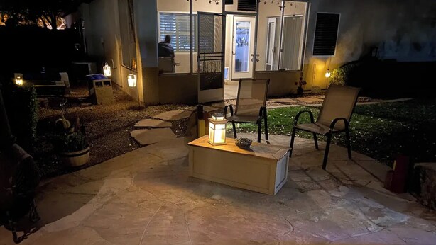 En udendørs patio med flisegulv, et lille bord med et stearinlys og udendørs møbler.