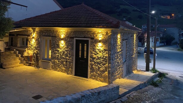 Edifici de pedra amb teulada aïllada, il·luminat per llums exteriors, situat a un carrer pavimentat amb un paisatge ondulat al fons.