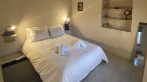 Un dormitori amb un llit, un ventilador de sostre, làmpades de nit, una prestatgeria penjada a la paret i una catifa amb dibuixos en blanc i negre.