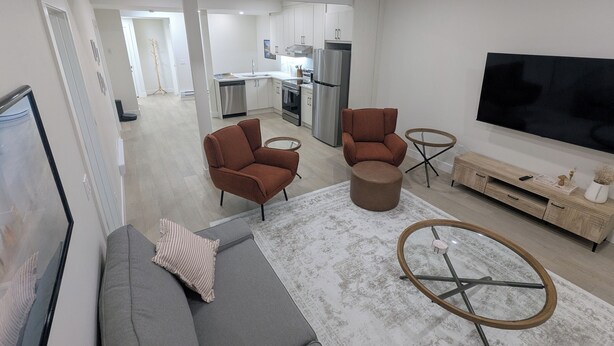 Una sala de estar moderna con un sofá gris, dos sillones marrones, una mesita de centro y un televisor sobre un mueble de madera.