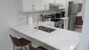 Una cocina moderna con encimeras de mármol blanco, electrodomésticos de acero inoxidable y taburetes de bar color café.