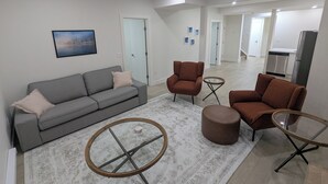 Una sala de estar moderna con un sofá gris, dos sillones marrones, una mesa de centro de vidrio y una alfombra estampada.