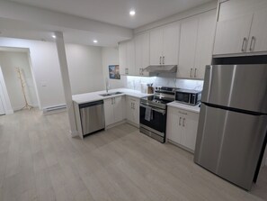 A modern kitchen with stainless steel appliances, white cabinetry, and a light wood floor. - {Greystone Retreat} Walk to River, Downtown, Rec Center (Cochrane)