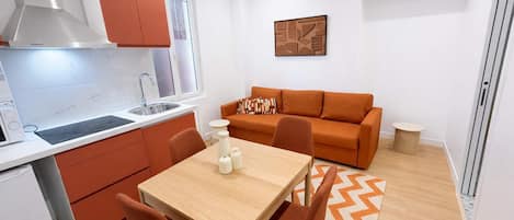 Een compacte leefruimte met een kitchenette, een eettafel met stoelen, een bank en een kleine ronde tafel.