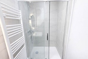 A modern bathroom with a glass-enclosed shower, white tiled walls, and a white towel rack. - Appartement Moderne Proche Paris Aubervilliers 4P (Aubervilliers)