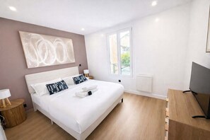 Een moderne slaapkamer met een groot bed, een televisie en een raam met uitzicht op groen.