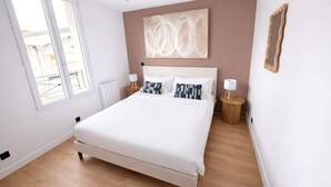 A bedroom with a large bed, two bedside tables, a window, and a wall-mounted artwork. - Appartement Cosy a Aubervilliers - 4P (Aubervilliers)