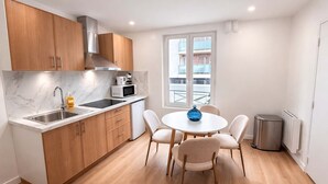 A compact kitchen with wooden cabinets, a built-in microwave, and a sink. There's a round table with chairs and a blue vase. - Appartement Cosy a Aubervilliers - 4P (Aubervilliers)