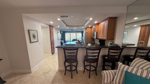 A spacious kitchen with a central island, wooden cabinets, and a dining area with striped cushions. - Cape coral/Fort Myers: First floor condo on wide canal next to Jaycee park (Cape Coral)