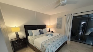 A bedroom with a bed, two bedside tables, a ceiling fan, a window with curtains, and a view of the outside. - Cape coral/Fort Myers: First floor condo on wide canal next to Jaycee park (Cape Coral)