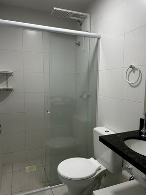Egy fürdőszoba üvegfalas zuhanyzóval, fehér WC-vel és fekete munkalapból készült mosdókagylóval.