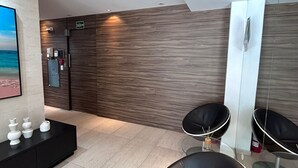 A modern waiting area with a black leather sofa, a glass coffee table, and a black console table with decorative items. - AP ENCANTADOR 1 QUARTO PX. DO CAU HANSEN (Joinville)