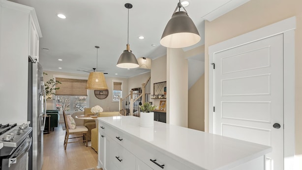 Una cocina moderna con armarios blancos, una isla central, iluminación colgante y vista al área de comedor.