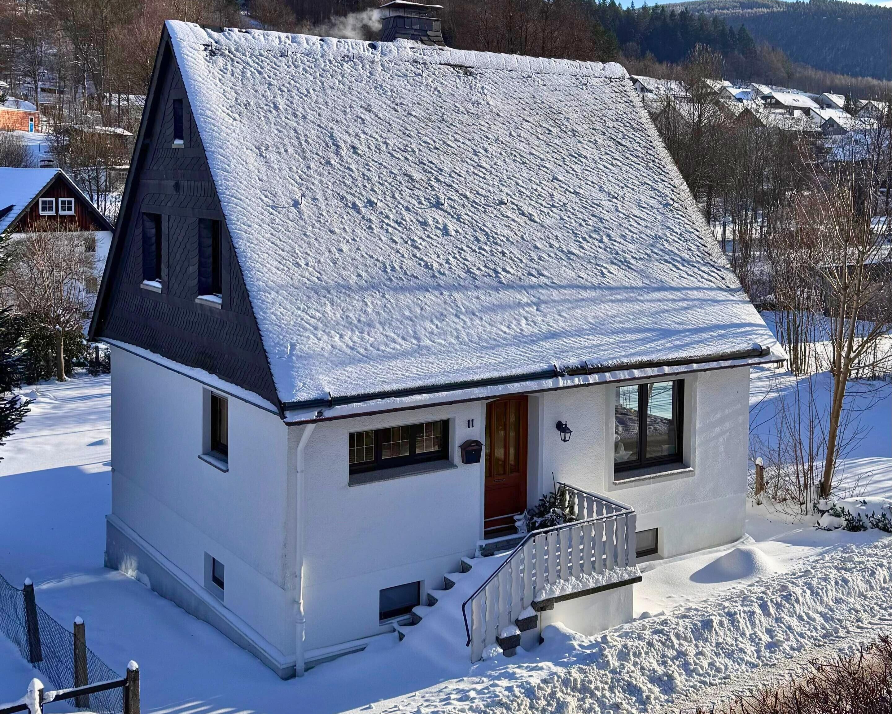 Et hvidt hus med et stejloppet tag, en lille veranda og en trappe til indgangen.