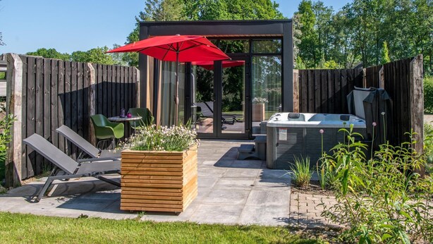 A backyard with a wooden deck, a hot tub, a red umbrella, and a seating area with chairs and a table. - Romantic Getaway at Drenthe Nature Lodge (Dalerveen)