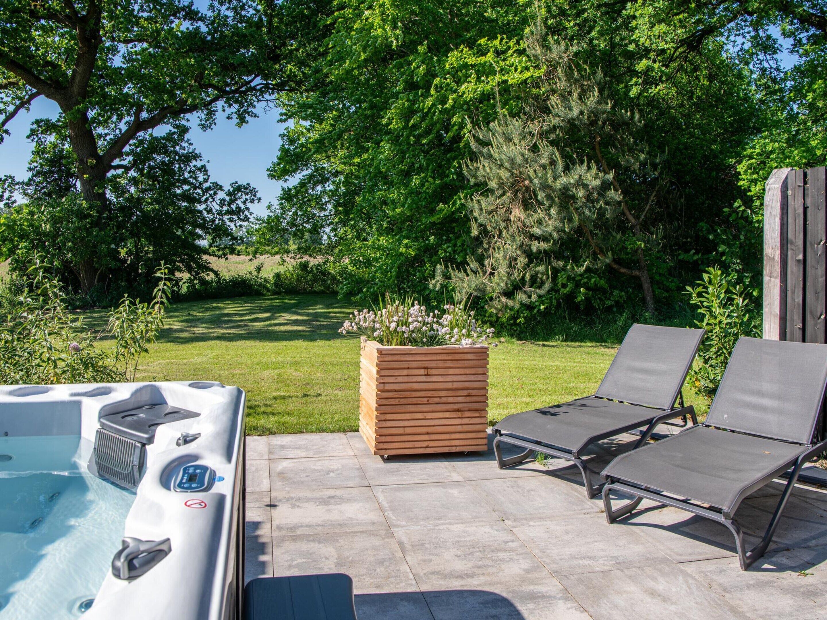 A hot tub with a control panel, two lounge chairs, and a wooden planter with flowers.