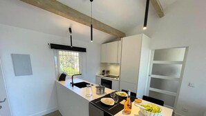 A modern kitchen with white cabinetry, a black countertop, and a dining area with a white table. - 🌅 ST CLAIR  LAVANDOU  EXCEPTIONAL PENTHOUSE  TOP FLOOR  180° PANORAMIC SEA VIEW (LE LAVANDOU)