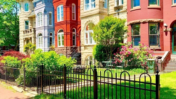 Une rangée de maisons de ville colorées, de style victorien, se distinguant par leurs éléments architecturaux particuliers, un jardin bien entretenu et une clôture en métal au premier plan.