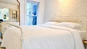 Une chambre avec un lit blanc, un tapis à motifs, un mur en briques blanches et un luminaire suspendu.