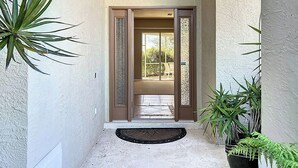 A building entrance with a glass door, a small porch area, and potted plants. - Butterfly House – Organic Garden Retreat in Popular Golf Community (Sarasota)
