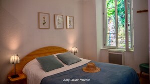 A bedroom with a wooden headboard, a bed with blue bedding, two wall-mounted lamps, and a window with a view of greenery. - Estate With Panoramic Sancy Views (Mont-Dore)