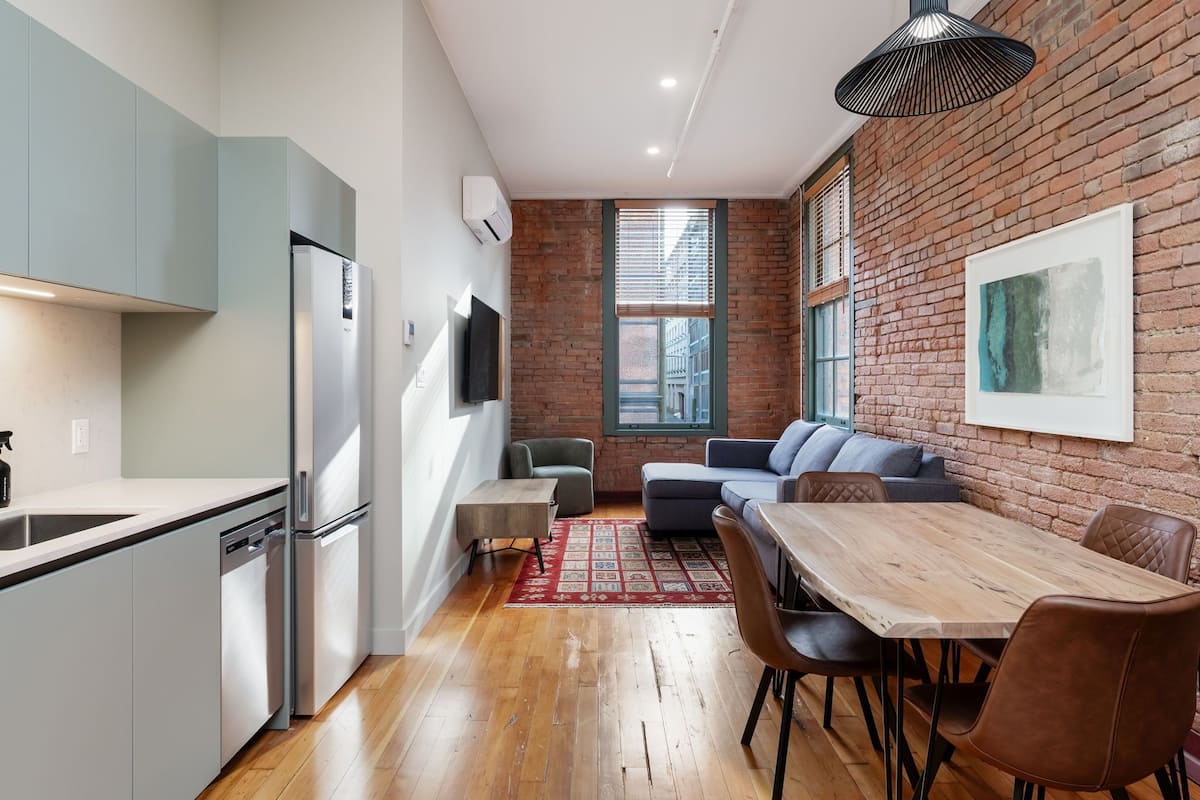 A modern kitchen with a refrigerator, dishwasher, and a dining area with a wooden table and chairs.