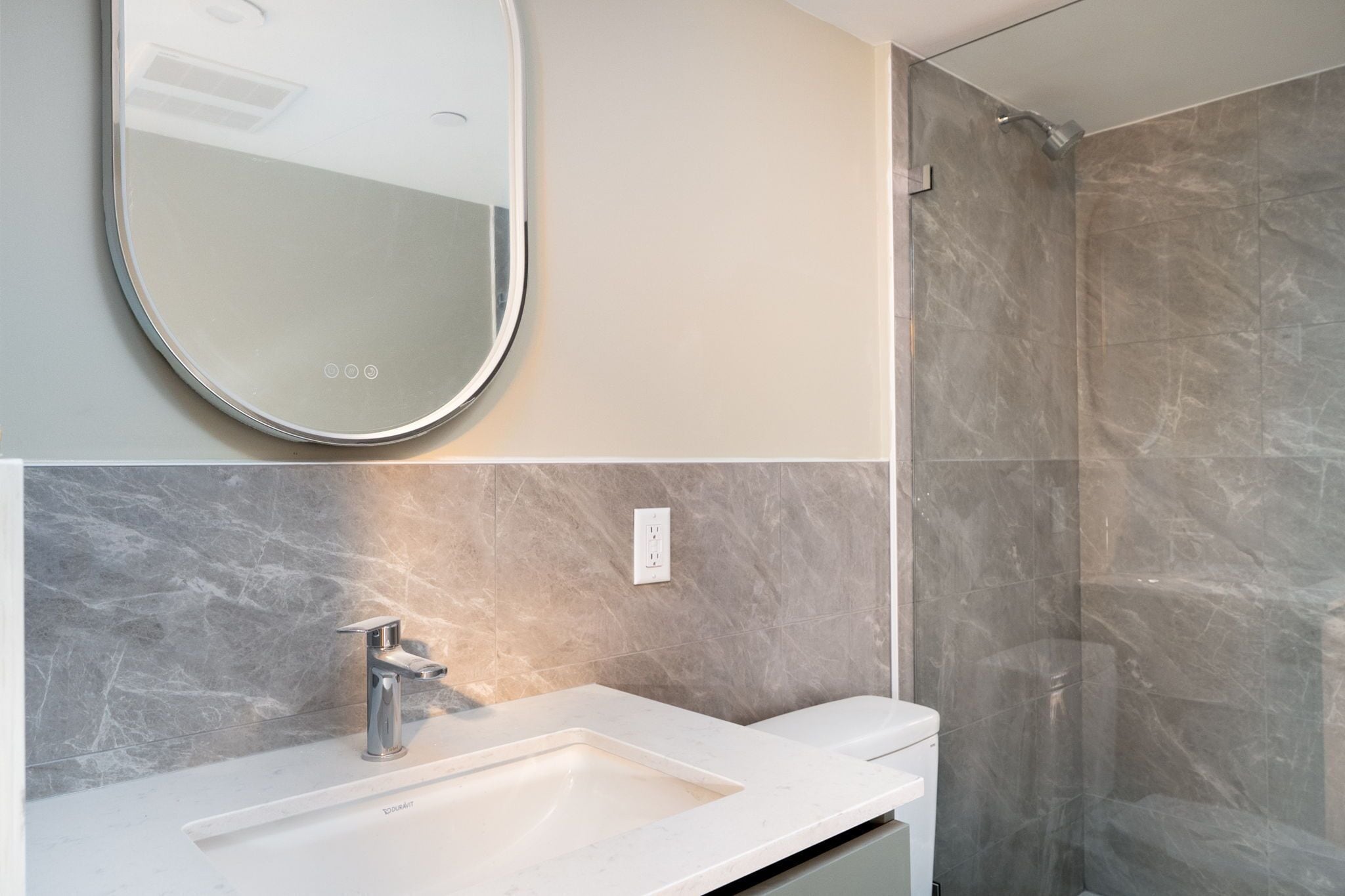A modern bathroom with a marble sink, a mirror, and a shower area.