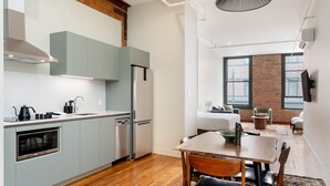 A modern kitchen with grey cabinets, a stainless steel refrigerator, and a dining area with a wooden table and chairs. - Block House (Vancouver)