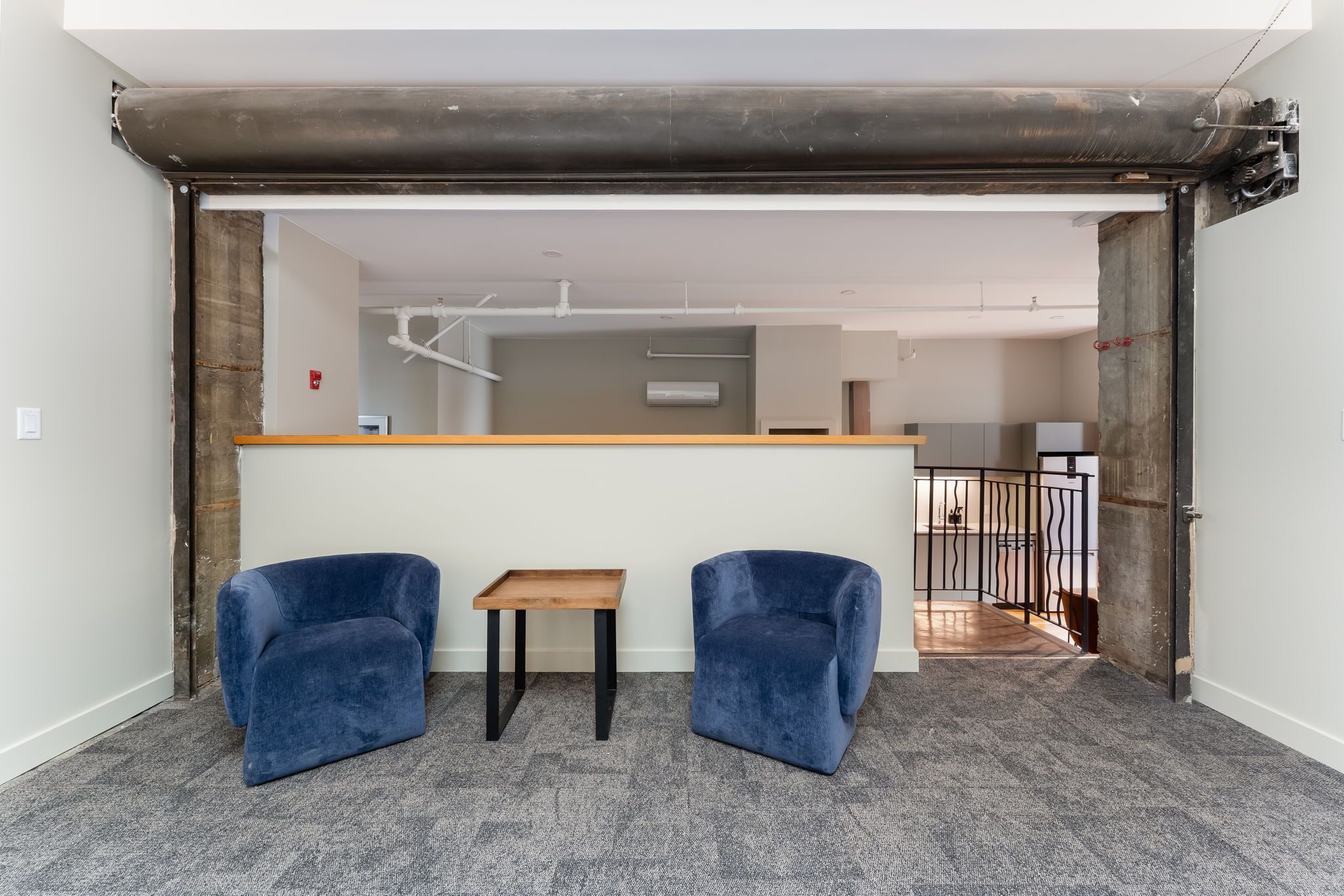A room with two blue chairs, a small wooden table, and a grey carpeted floor.