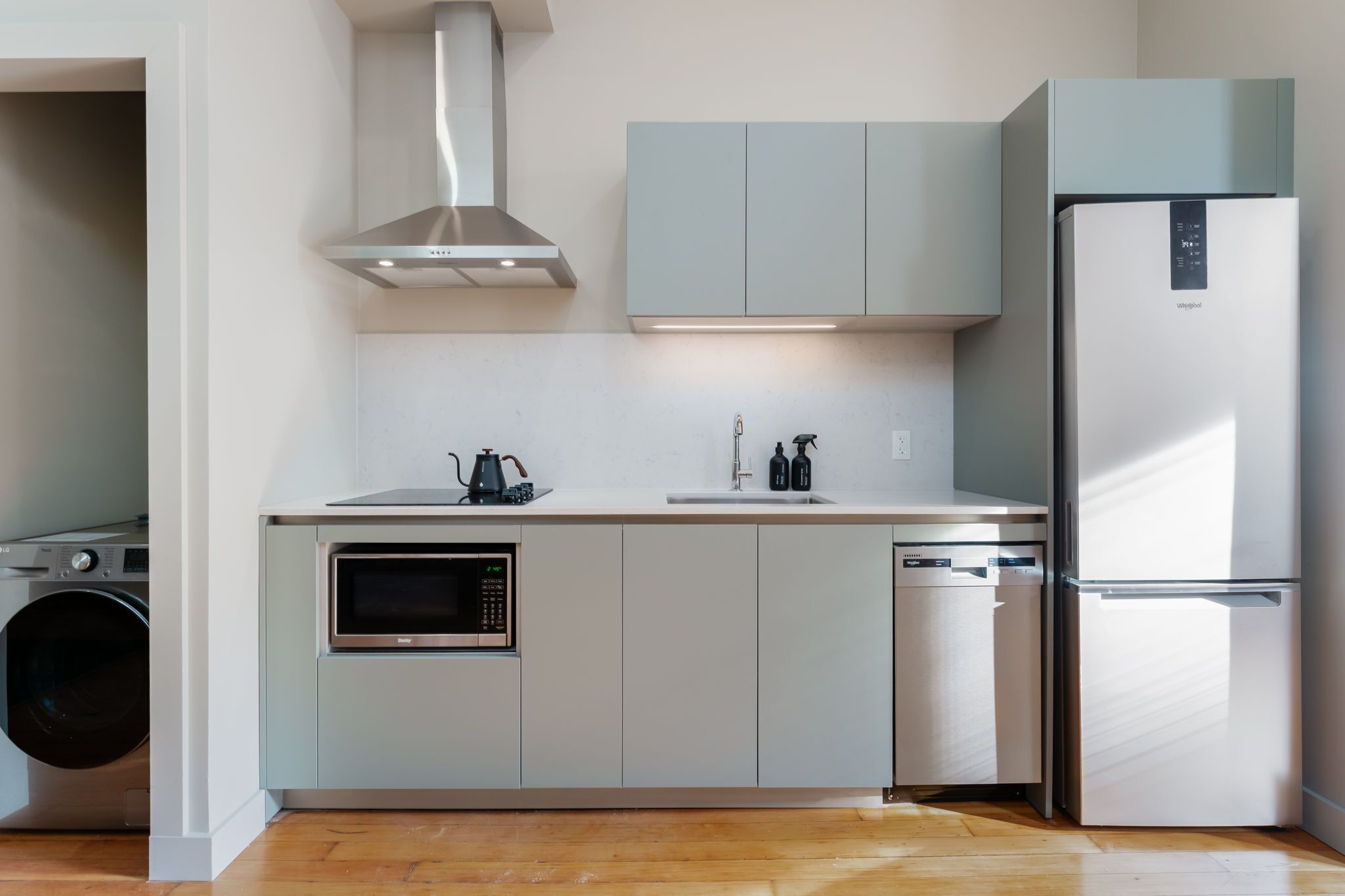Een moderne keuken met een ingebouwde wasmachine, magnetron, vaatwasser en een roestvrijstalen koelkast.