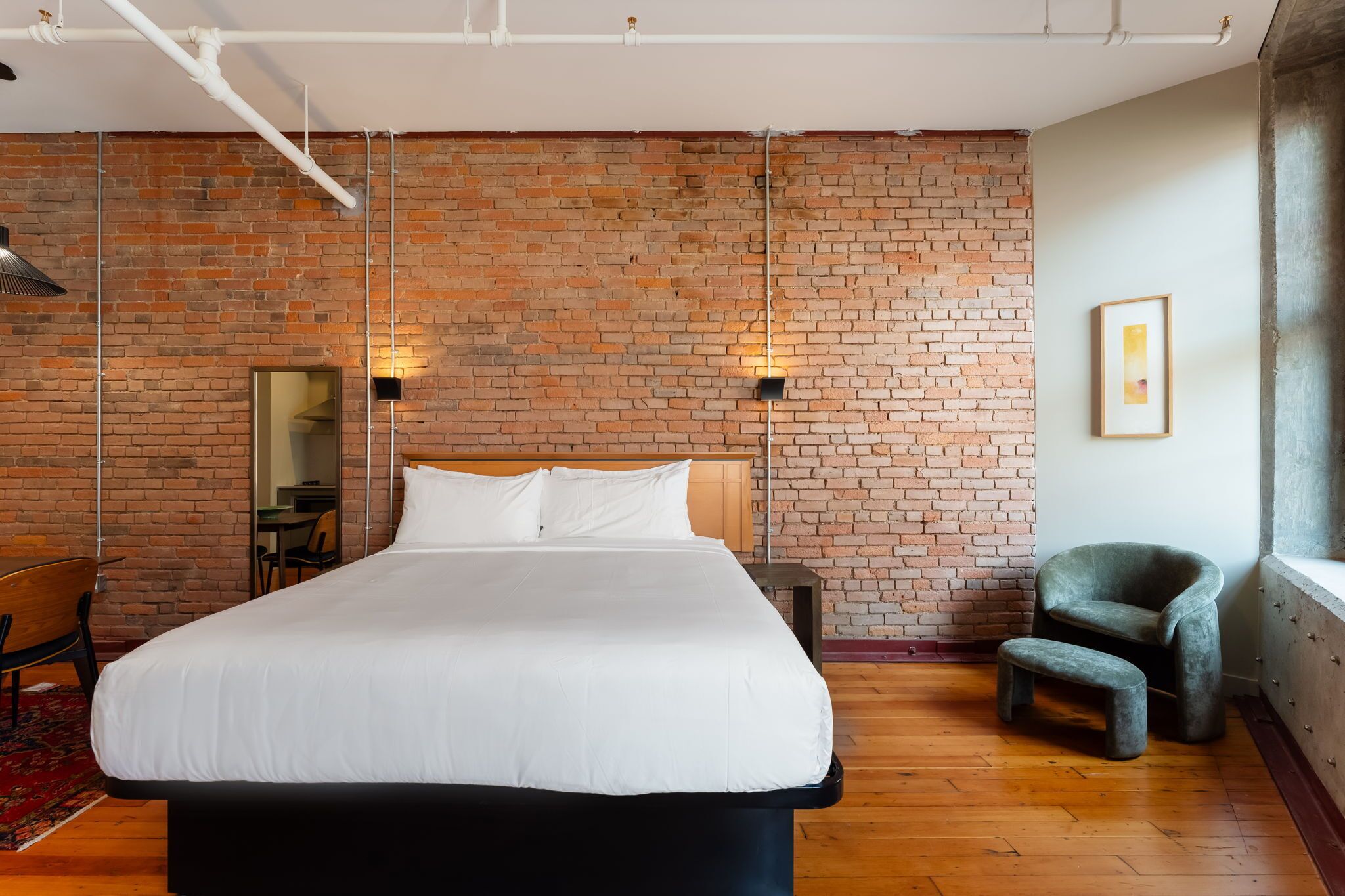 Ein Hotelzimmer mit einem großen Bett, einer Ziegelwand, einem kleinen Tisch, einem Stuhl und einem Fenster.
