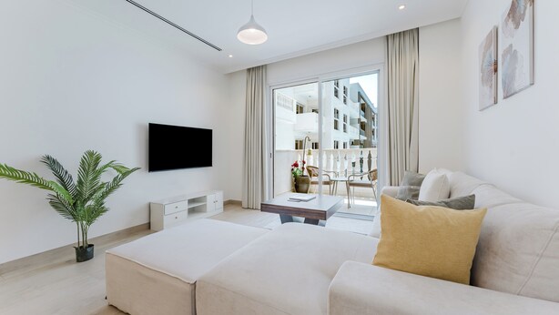 Ein modernes Hotelzimmer mit einem Flachbildfernseher, einer Sitzecke, einem Esstisch und einem Balkon mit Blick auf das Gebäude.