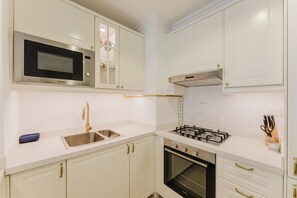 Una cocina con armarios blancos, un lavamanos de acero inoxidable, un microondas, una estufa y un horno.