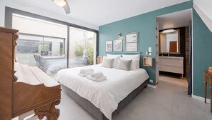 Ein modernes Schlafzimmer mit einem großen Bett, einem Deckenventilator, einem Badezimmer mit Spiegel und Blick ins Freie.