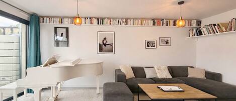 A modern living room with a piano, a grey sofa, a coffee table, and a bookshelf filled with books.