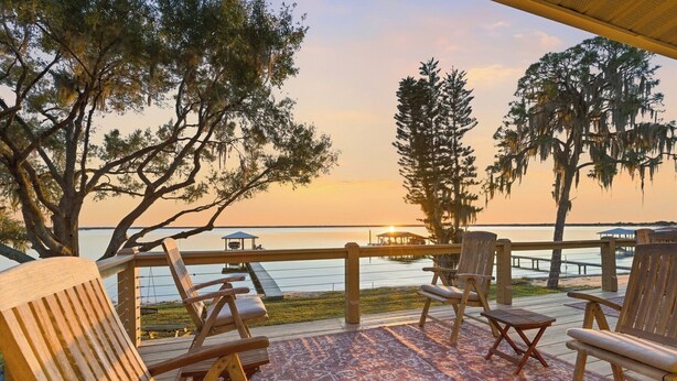 A wooden deck with outdoor seating, overlooking a calm body of water at sunset. - Golden Hour on Lake June - Dock, Deck & Views (Lake Placid)