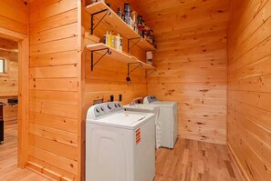A wooden cabin interior with a laundry area featuring two washing machines and shelves stocked with various items. - New Cabin with Breathtaking View (Boone)