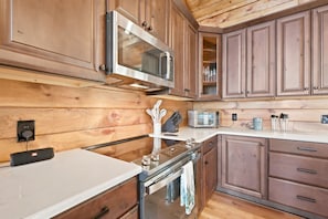 A kitchen with wooden cabinets, a microwave, a toaster, and a stove. - New Cabin with Breathtaking View (Boone)
