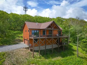 A wooden cabin with a balcony, surrounded by lush greenery and a clear sky. - New Cabin with Breathtaking View (Boone)