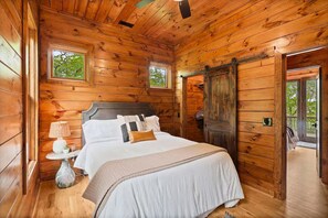 Une chambre à coucher située dans une cabane en bois, avec un lit, une lampe de chevet et deux fenêtres.