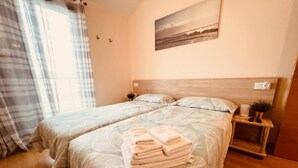 A hotel room with two beds, a bedside table with a plant, a painting on the wall, and a window with curtains. - Sol, Golf & Relax – Luxury house golf & sea (San Jorge)