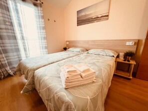 A hotel room with two beds, a bedside table with a plant, a painting on the wall, and a window with curtains. - Sol, Golf & Relax – Luxury house golf & sea (San Jorge)