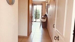 A hallway with a door, a wall-mounted light fixture, and a view into a room with a window and a chair. - Sol, Golf & Relax – Luxury house golf & sea (San Jorge)