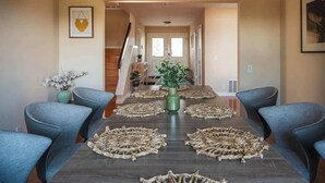 Uma sala de jantar com uma mesa comprida, cadeiras azuis e jogos americanos trançados.