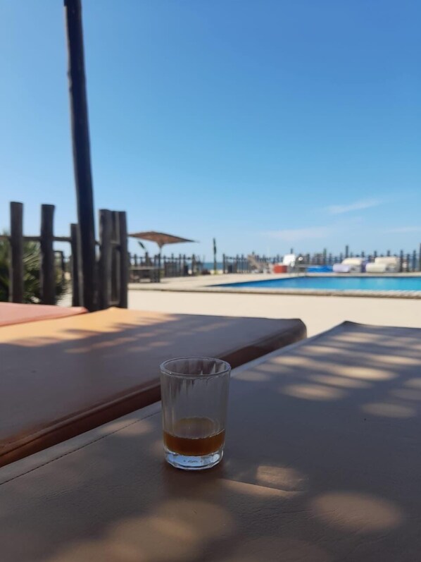 Ein Glas mit einem Getränk auf einem Holztisch, mit Blick auf einen Swimmingpool und einen klaren Himmel.