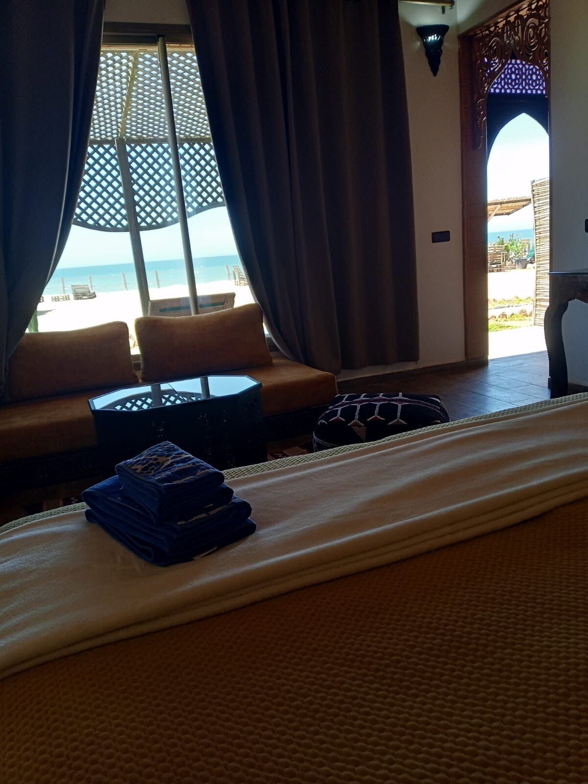 A hotel room with a bed, a sofa, a small table, and a view of the beach.