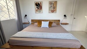 A bedroom with a wooden bed, two wall-mounted nightstands, a window with curtains, and abstract wall art.