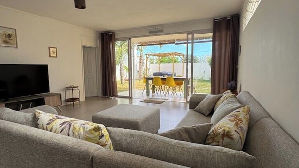 A modern living room with a sofa set, a flat-screen TV, and a sliding glass door leading to an outdoor patio with yellow chairs.